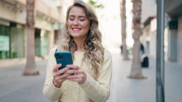 Young blonde woman tourist smiling confident using smartphone at street