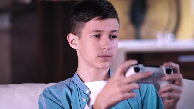 serious teen boy sitting on the sofa and plays a game on a console, cinematic shot