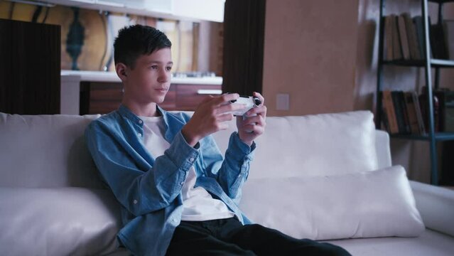 serious teen boy sitting on the sofa and plays a game on a console, cinematic