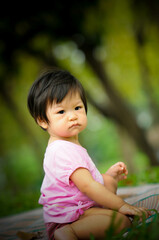 Cute baby Thai girl feel happy and relaxing , sitting on the grass in the park