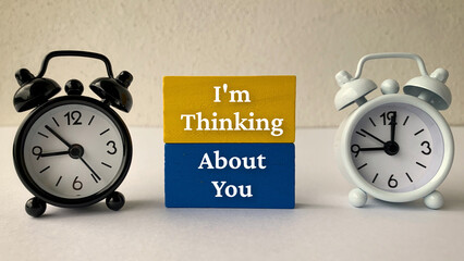 I am thinking about you text on wooden blocks with alarm clocks background.