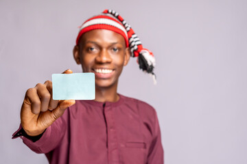 african man wearing african attire dress holding id card mock up stands on a grey studio wall ....