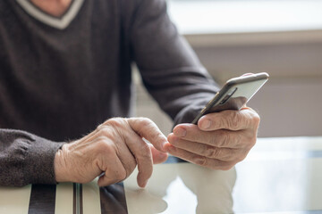 Elderly man dials number in smartphone from home. Old senior sends sms on mobile phone. High quality photo