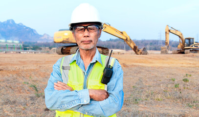 Asian senior male engineer wearing safety vest and helmet inspects civil works The chief construction engineer uses a walkie-talkie to manage the excavator.