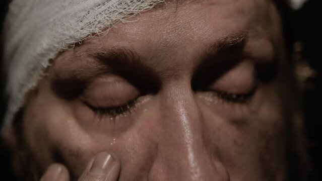War, accident, crying man. Close-up of eyes with tears of scared injured man with dirty face and bandaged head. Slow motion