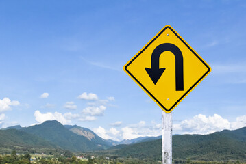 Traffic sign: left U-turn sign on cement pole beside the rural road with white cloudy bluesky background, copy space.
