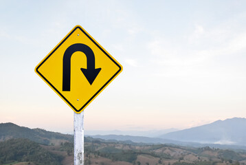 Traffic sign: Right U-turn sign on cement pole beside the rural road with white cloudy bluesky...