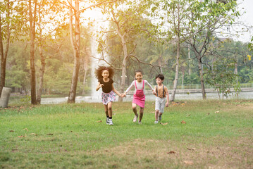 Naklejka na ściany i meble Small group of a happy children run through the park in the background of grass and trees. Children's outdoor games, vacations, weekend, Children's Day