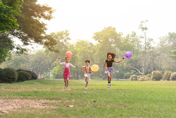 Fototapeta premium Small group of a happy children run through the park in the background of grass and trees. Children's outdoor games, vacations, weekend, Children's Day