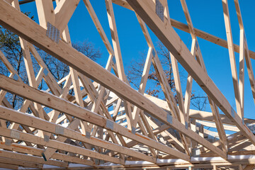 Many wooden roof trusses on a new home construction project with blue sky in the background.