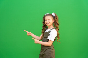 A child with curly hair points to an advertisement. A little girl with curly hair points to your ad standing on an isolated green background.