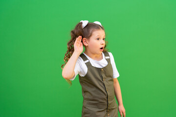 Little children is eavesdropping on conversations. The girl holds her hand near her ear and listens.