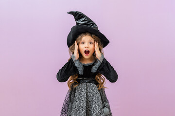 A surprised and joyful sorceress in a black fancy dress on an isolated background. A little girl in a witch costume with curly hair.