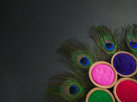 colorful powders for holi on clay pots on occasion of indian festival of colors. happy holi theme shot against black background with peacock feathers.