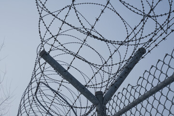 Prison fence against blue sky closeup. Barbed wire. Restricted area. Classified state zone.