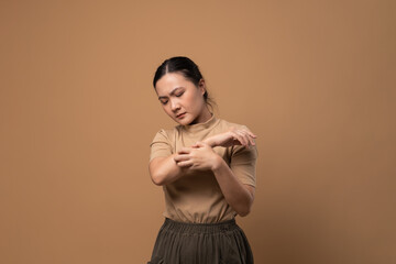 Asian woman was sick with irritate itching her skin standing isolated on beige background.