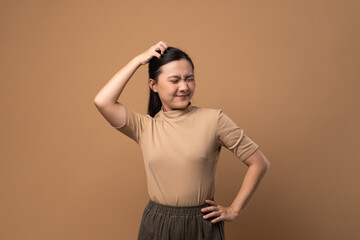 Asian woman scratching her head, standing isolated on beige background.