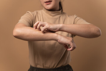 Asian woman was sick with irritate itching her skin standing isolated on beige background.