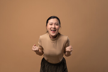 Asian woman happy make a winning gesture isolated on beige background.