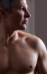 Naklejka premium Sculpted and thoughtful. A darkly lit image of a shirtless man looking away thoughtfully.