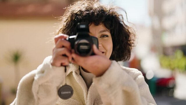 Young hispanic woman smiling confident using professional camera at street