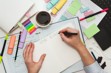 Student desk. The girl makes notes on stickers in the study schedule. The process of homeschooling or preparing homework . Top view of the table with student stationery and notes.