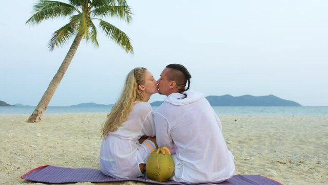 Loving couple in white dress, near palm tree, kissing, relax and drinking coconat cocktail Pina Colada. Concept sea beach resting tropical tourism summer holidays wedding love family vacations
