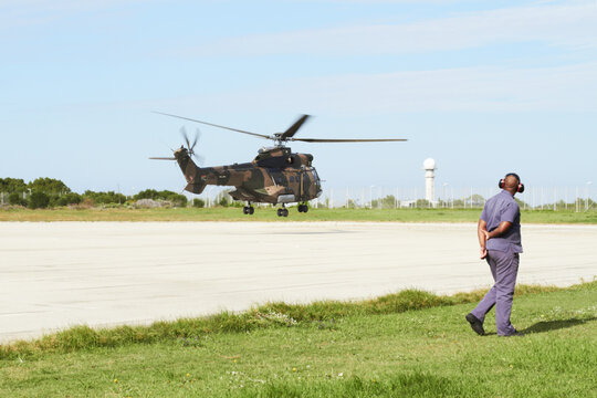 Coming in for a land. A helicopter landing on a launchpad while an officer stands on the side.