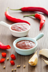 Bowl of hot chili sauce with red peppers on dark wooden background,