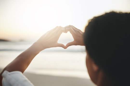 I love anything with a beautiful view. Rearview shot of a woman woman forming a heart against the horizon at the beach.