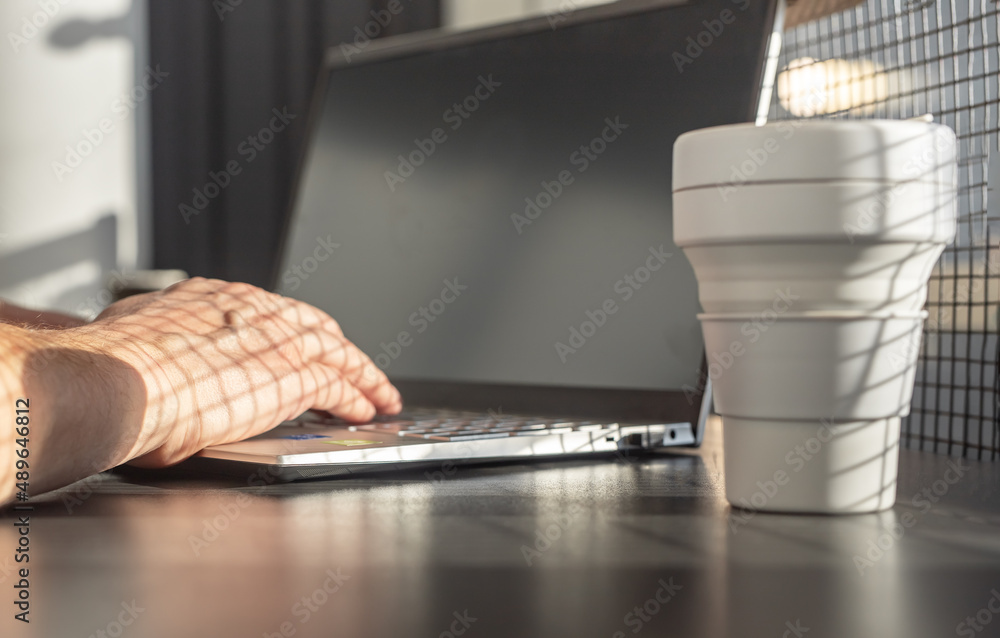 Poster Man hands closeup typing on laptop keyboard. Businessman or student sitting at table with computer and takeaway eco silicon cup and working or studying. High quality photo