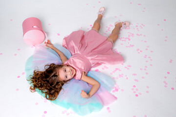 Obraz na płótnie Canvas beautiful little girl in a chic pink dress lies on the floor strewn with confetti. top view