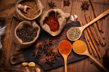 Spices and herbs raw material for cooking in wooden spoon and wooden plate with dark tone.