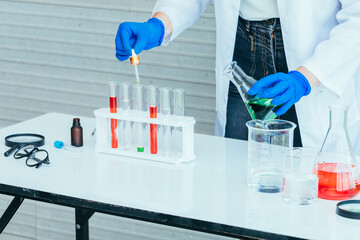 Hand of Scientist in uniform holding beaker and test tube have chemical liquid for testing chemical reaction.