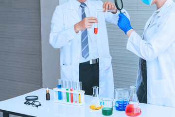 Scientist team in uniform holding beaker and test tube have chemical liquid for testing chemical reaction.