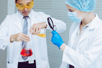 Scientist team in uniform holding beaker and test tube have chemical liquid for testing chemical reaction.