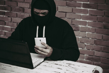 Anonymous hacker using laptop and smartphone for stealing personal data from internet.