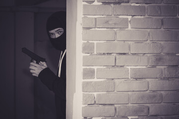 Thief wear cover faces and black jacket  with gun is hiding behind the old wall.