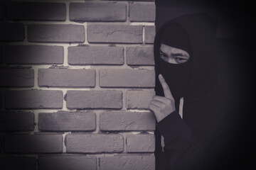 Thief wear cover faces and black jacket is hiding behind the old wall.