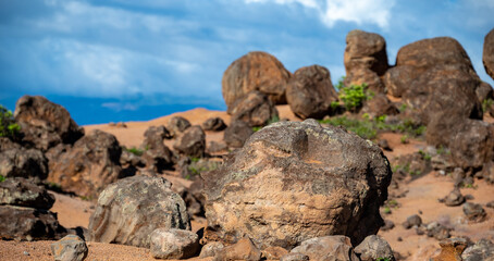 Fototapeta na wymiar A scene of boulders and rocks on a hill of red clay dirt, blue sky above, in this rugged scene of the Garden of the Gods on the island of Lanai, Hawaii. 