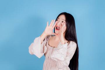 Cheerful asian young woman shouting. yelling with hand close up on blue background.