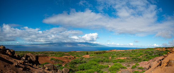 Looking across a rugged landscape  on Lanai of red dirt, growing shrubs and boulders to the ocean...
