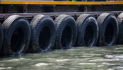 Row of black car tires used as boat bumpers at pier.