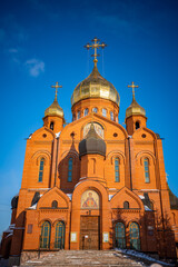 Fototapeta na wymiar Kemerovo, Russia - February 26, 2022: Brick cathedral Orthodox church with crosses under a blue sky in Kemerovo city in Siberia, Russia