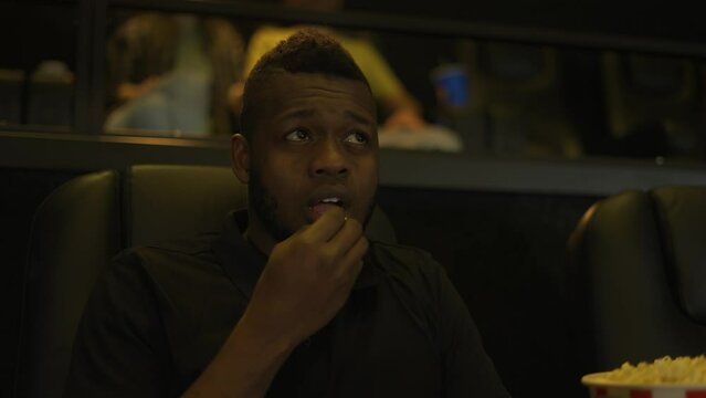 African American man sitting in armchair watching a horror movie at the cinema, scary face