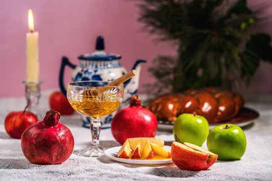 Apples, pomegranates, honey and wicker challah on table.
