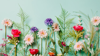 Various field flowers and fresh leaves in a row on pastel green background. Creative floral spring...