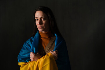Sad woman covered with Ukraine flag. Concept of standing with Ukrainian nation in war with Russia.