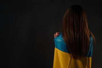 Rear view of woman covered with Ukraine flag. Concept of standing with Ukrainian nation in war with...