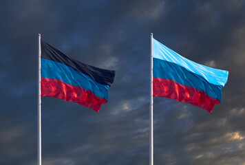 Flags of the Donetsk and Lugansk People's Republics against a dark cloudy sky.